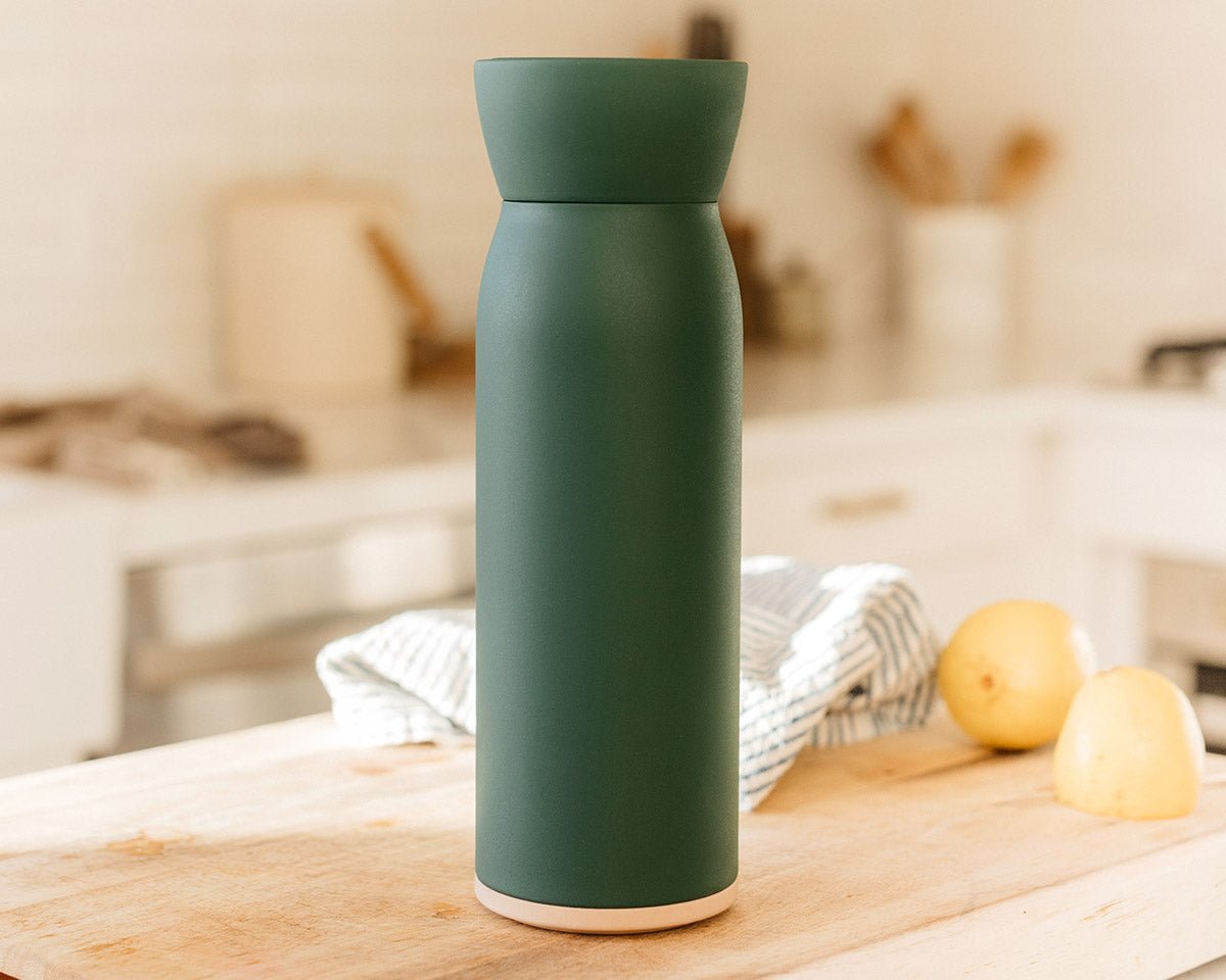 Hitch Bottle and Cup in Forest Green on wooden kitchen table with two lemon halves