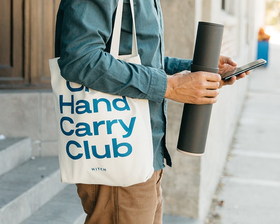 Man holding stacked Hitch Bottle and Cup in Charcoal gray with One Hand Carry Club Canvas Tote 