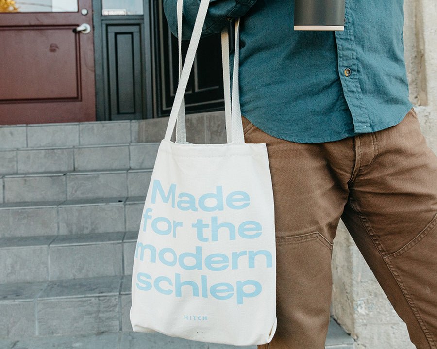 Man Carrying Canvas Hitch Tote with Made for The Modern Schlep printed in light blue, made in america