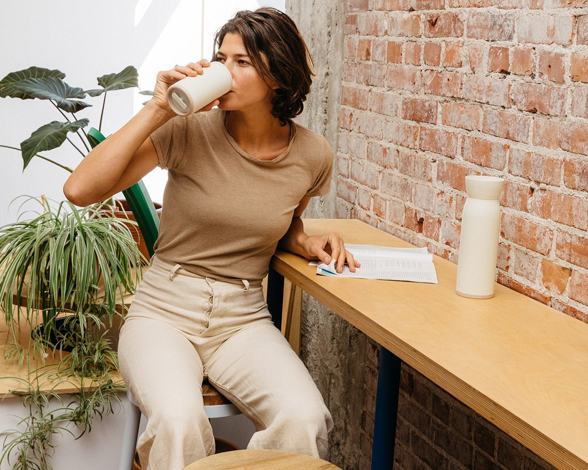 Woman sipping from barista-approved Hitch Cup in a coffee shop with exposed brick and indoor plants